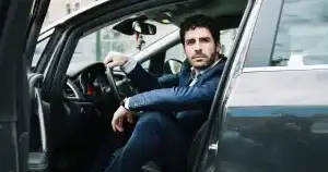 Un chauffeur professionnel en costume, assis dans son véhicule, prêt à démarrer.
